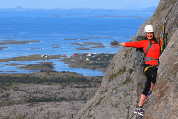 Klatring Via Ferrata i Ravnfloget på Vega. Helgelandskysten i bakgrunnen, klatrer i fjellveggen.